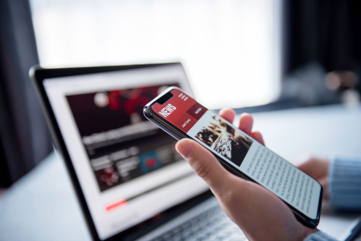 Person reading online news on a smartphone and laptop (Getty Images/oatawa)