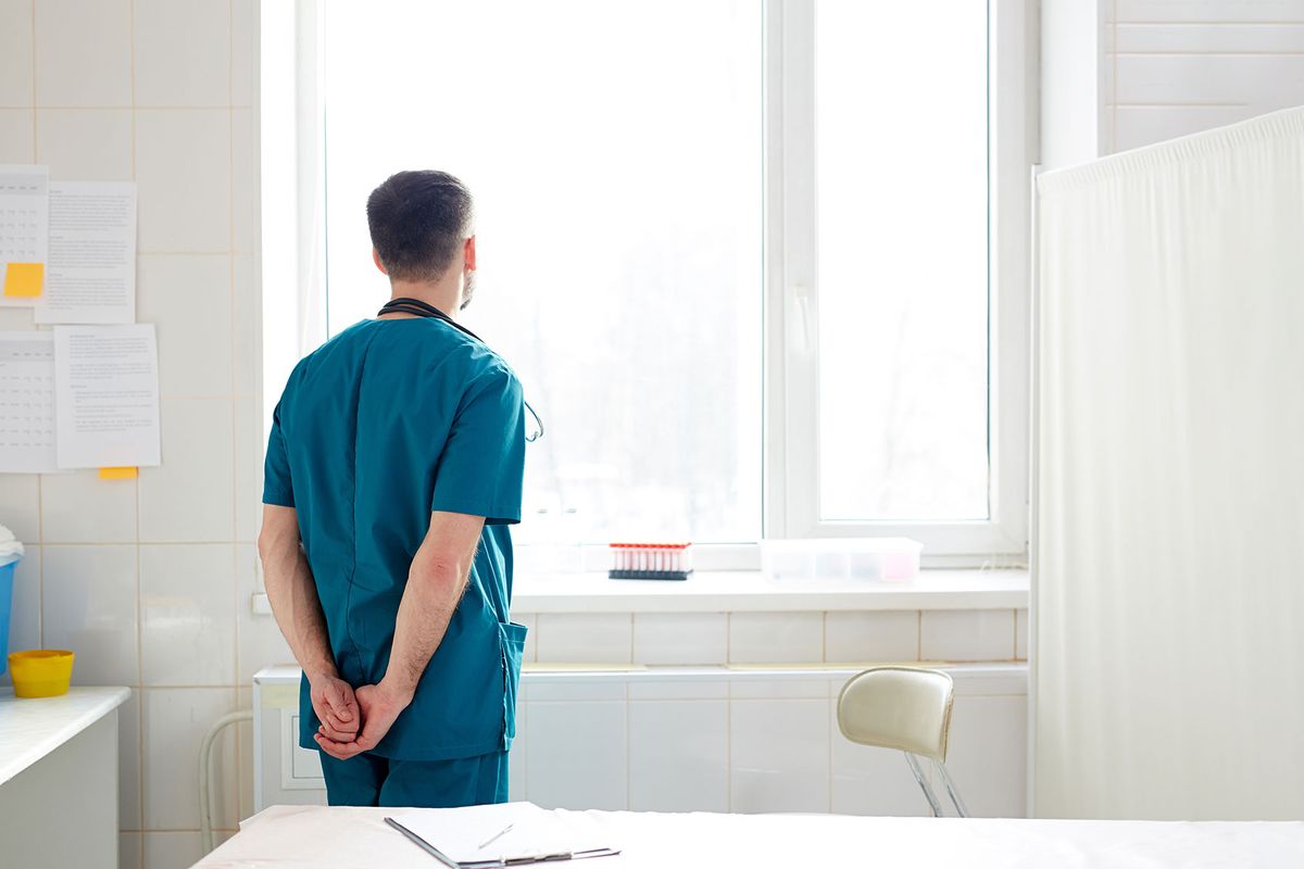 Clinician looking out window in a hospital (Getty Images/shironosov)