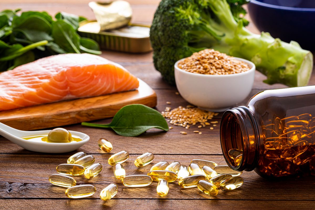 Front view of fish oil capsules spilling out from a bottle surrounded by an assortment of food rich in omega-3 such as salmon, flax seeds, broccoli, sardines, spinach, olives and olive oil.
 (carlosgaw / Getty Images)