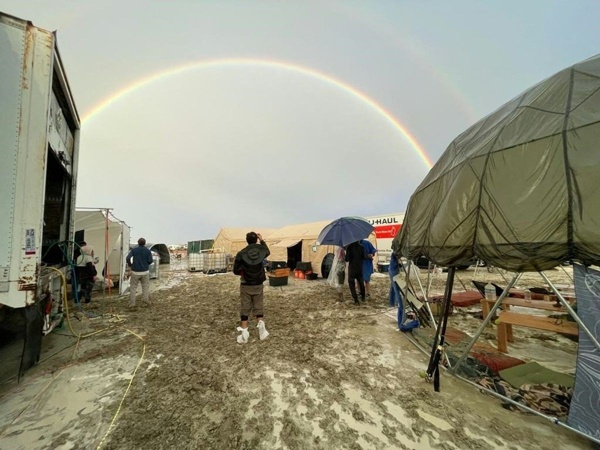 Attendees look at a rainbow over flooding on a desert plain on September 1, 2023, after heavy rains turned the annual Burning Man festival site in Nevada's Black Rock desert into a mud pit.  (Photo by JULIE JAMMOT/AFP via Getty Images)