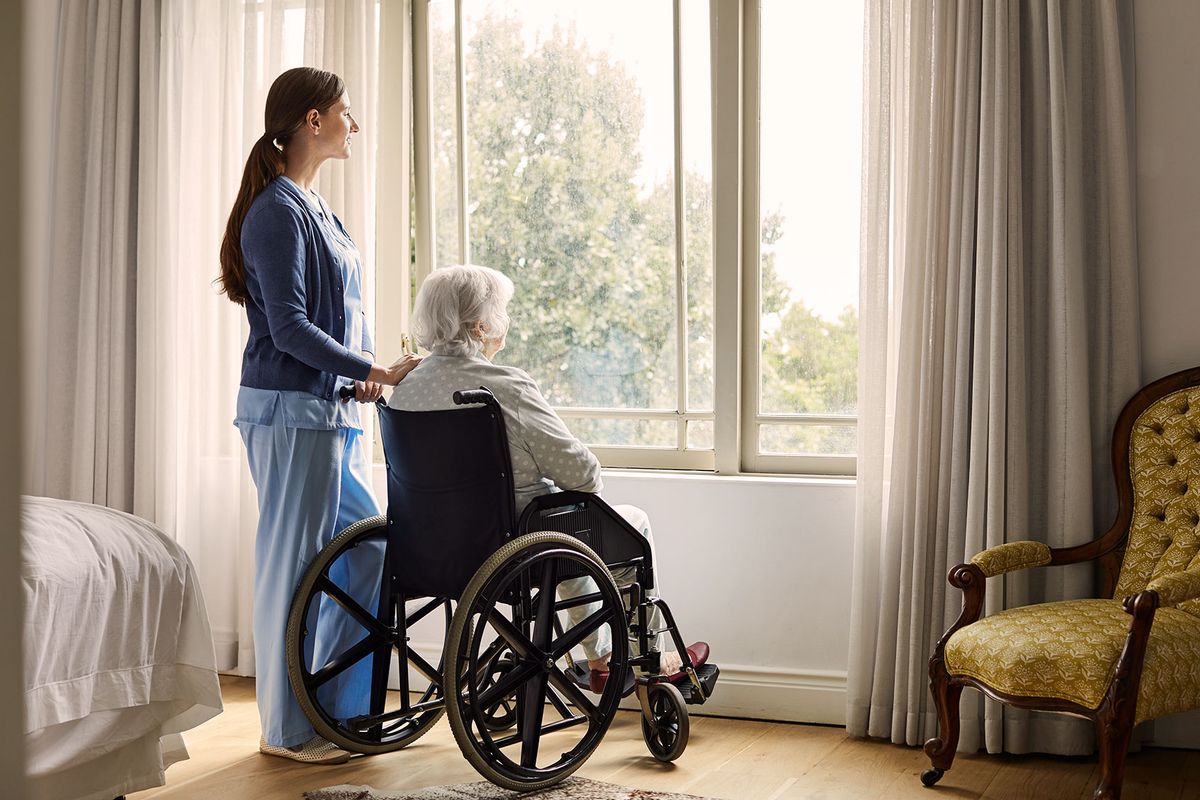 Nurse standing by elderly woman sitting on wheelchair (Getty Images/Morsa Images)