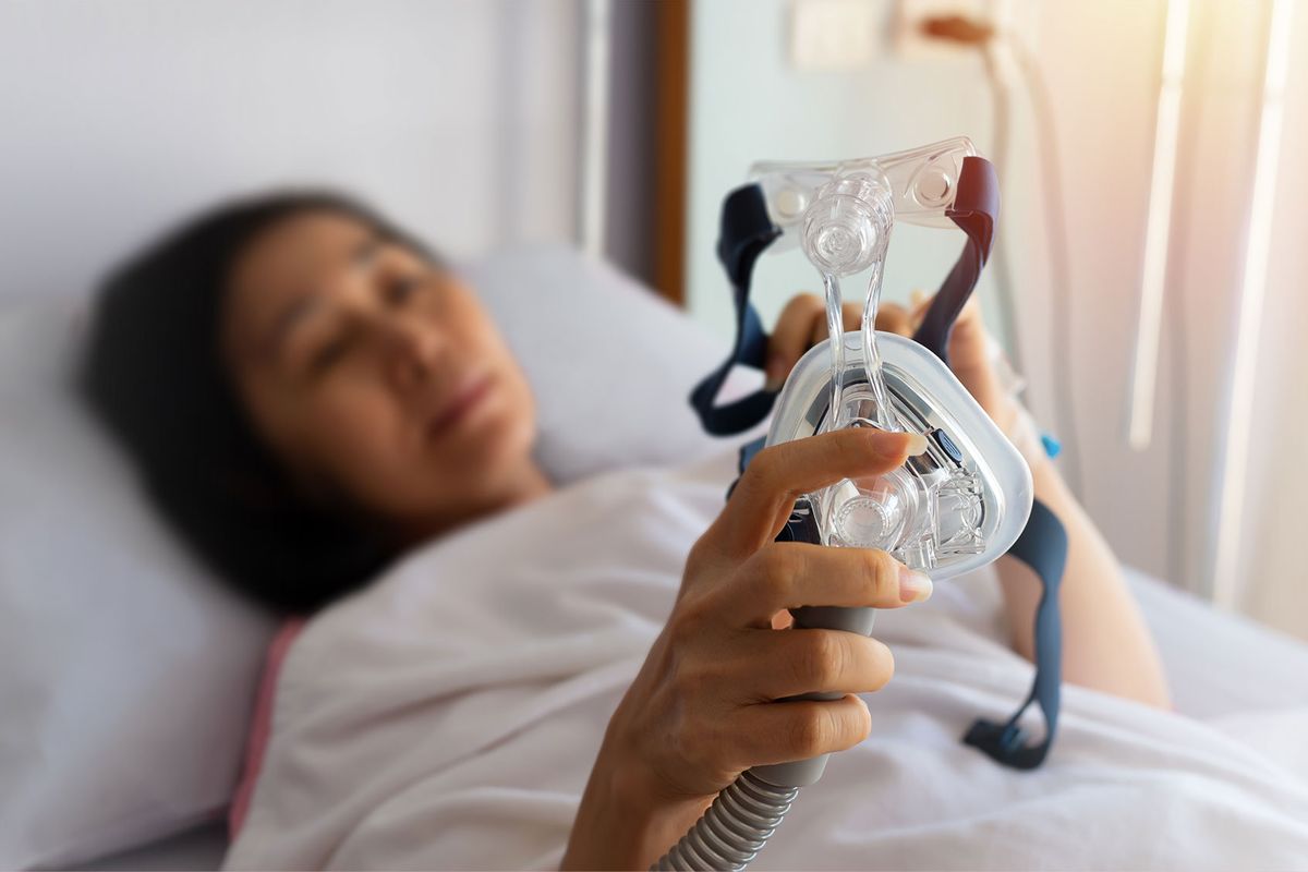 Patient holding CPAP machine mask (Getty Images/cherrybeans)