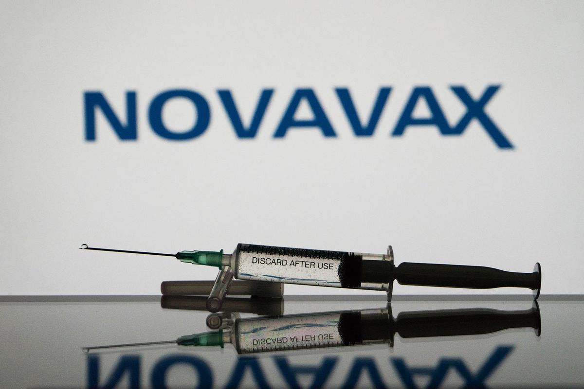 A covid-19 vaccine is seen with the Novavax logo in the background. (Photo Illustration by Nikos Pekiaridis/NurPhoto via Getty Images)