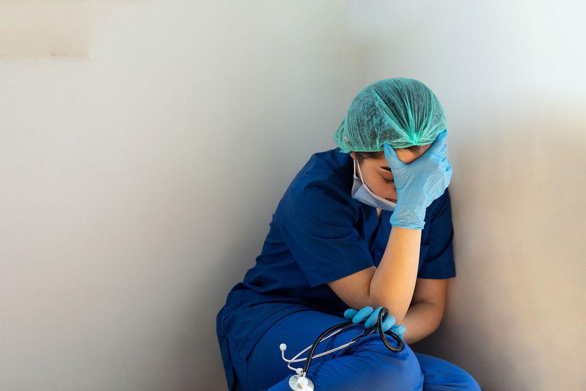 Tired healthcare worker sitting on the floor (Getty Images/bymuratdeniz)