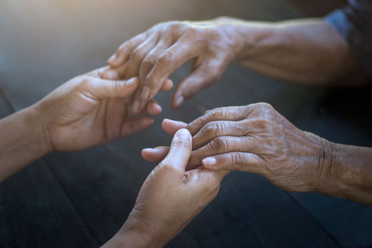 Young woman and elderly woman holding hands (Getty Images/ipopba)