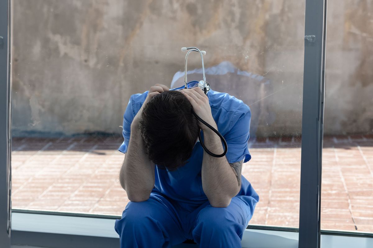 Male nurse sits in a modern hospital setting struggling with the long hours and enormous pressures. (Getty Images/Malachite Photography)