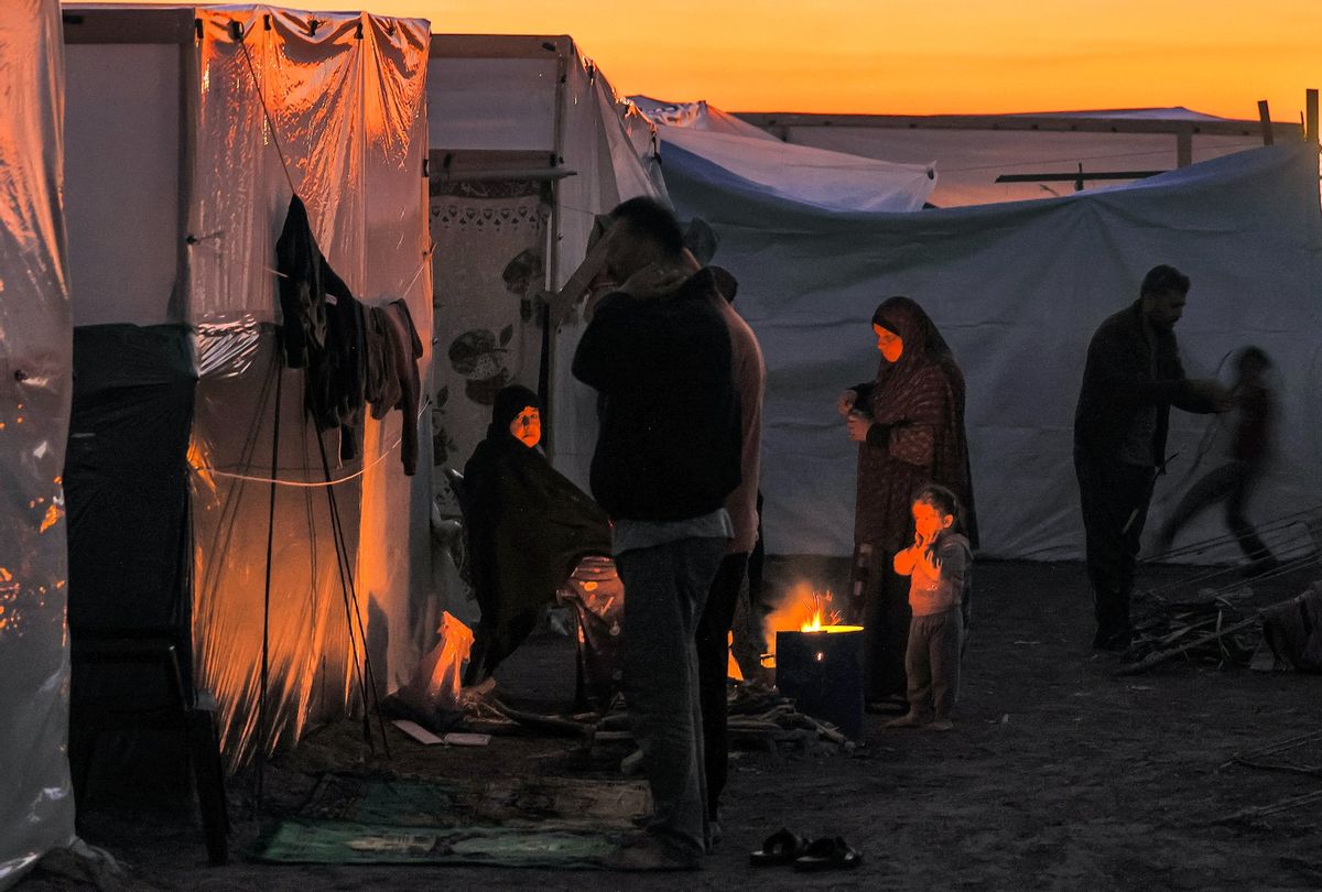 Men pray at sunset as people sit by a fire outside one of the tents housing Palestinians displaced by the conflict in Gaza between Israel and the Palestinian Hamas movement, in Rafah in the southern Gaza Strip on December 18, 2023. (MAHMUD HAMS/AFP via Getty Images)