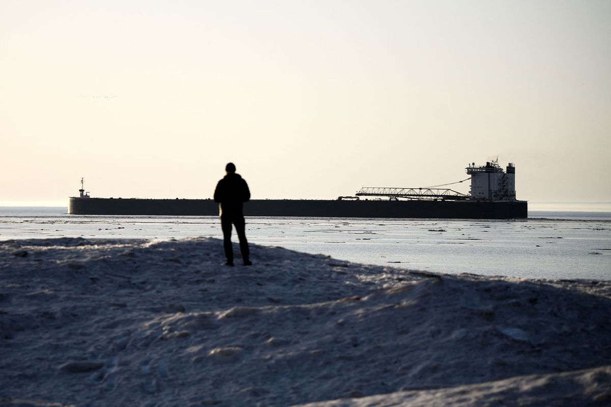 A person watches a shipping vessel from a mound of ice and snow on the shore of Lake Superior as the sun rises in Duluth, Minnesota, on April 13, 2023. (STEPHEN MATUREN/AFP via Getty Images)