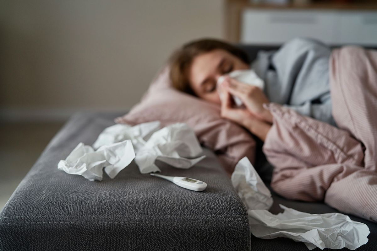 Young woman with high temperature and flu lying down on sofa (Getty Images/gpointstudio)