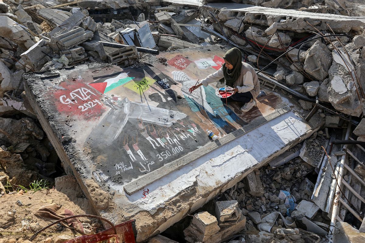 Palestinian female artist is seen drawing a picture titled 'GAZA 2024' on the concrete of the rubble of a destroyed building to draw attention to the losses and destruction caused due to Israeli attacks in Rafah, Gaza on January 01, 2024. (Abed Rahim Khatib/Anadolu via Getty Images)