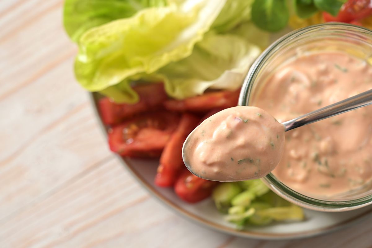 Thousand Island dressing on a spoon and in a glass jar over slices of lettuce and tomato. (Getty Images/fermate)