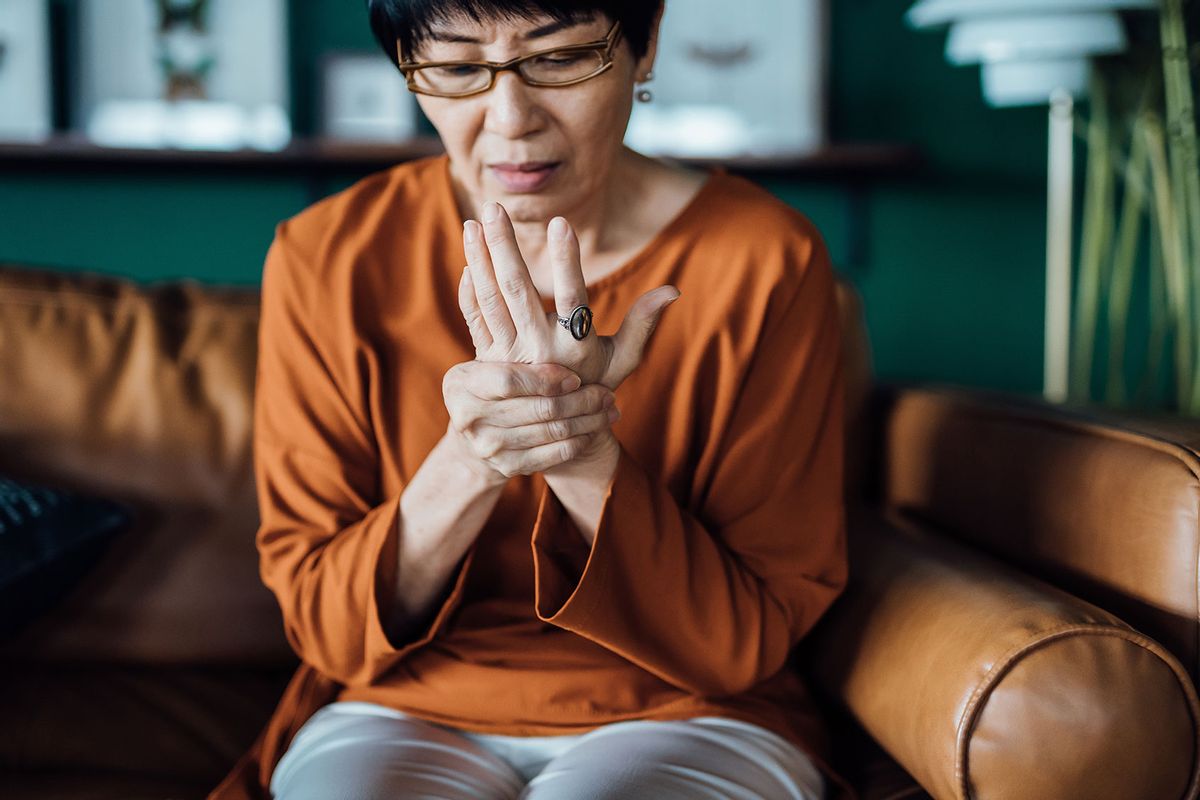 Senior Asian woman rubbing her hands in discomfort, suffering from arthritis in her hand while sitting on sofa at home. (Getty Images/AsiaVision)