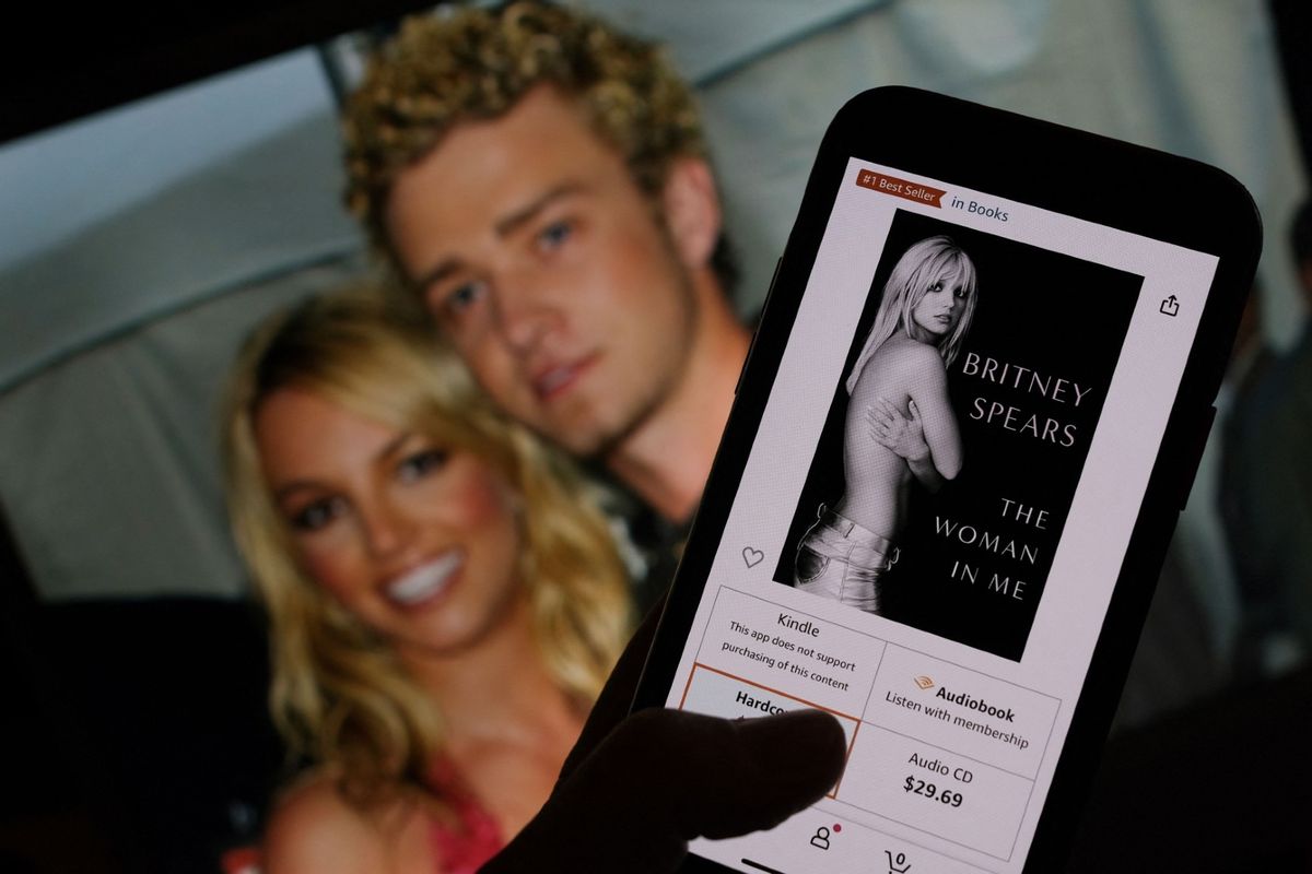 This illustration image taken on October 21, 2023 shows the cover of Britney Spears' book "The Woman in Me" from an online retailer in front of a picture of Britney Spears and Justin Timberlake at the American Music Awards from January 9, 2002.  ( CHRIS DELMAS/AFP via Getty Images)