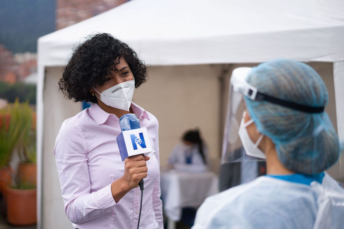 Journalist interviewing a healthcare worker working at a COVID-19 vaccination stand (Getty Images/andresr)