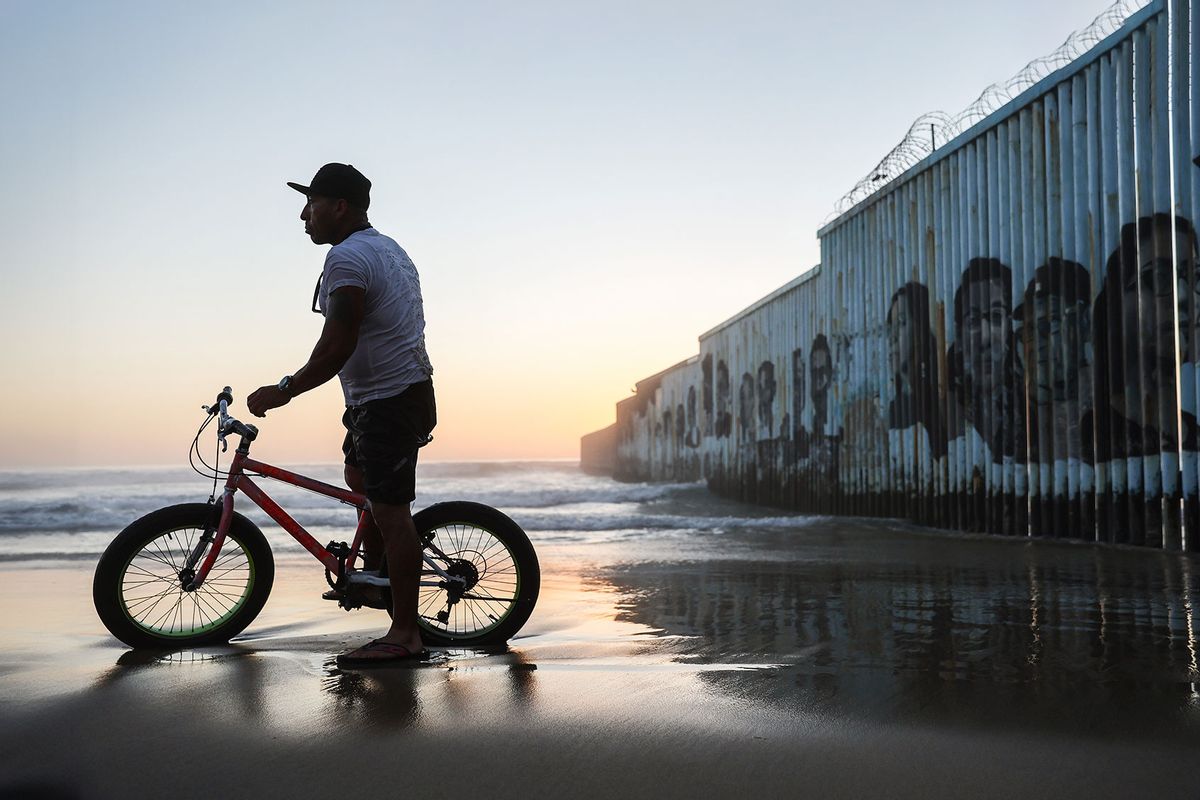 A cyclist stands on the beach near the U.S.-Mexico border barrier which extends into the Pacific Ocean on April 7, 2022 in Tijuana, Mexico. (Mario Tama/Getty Images)