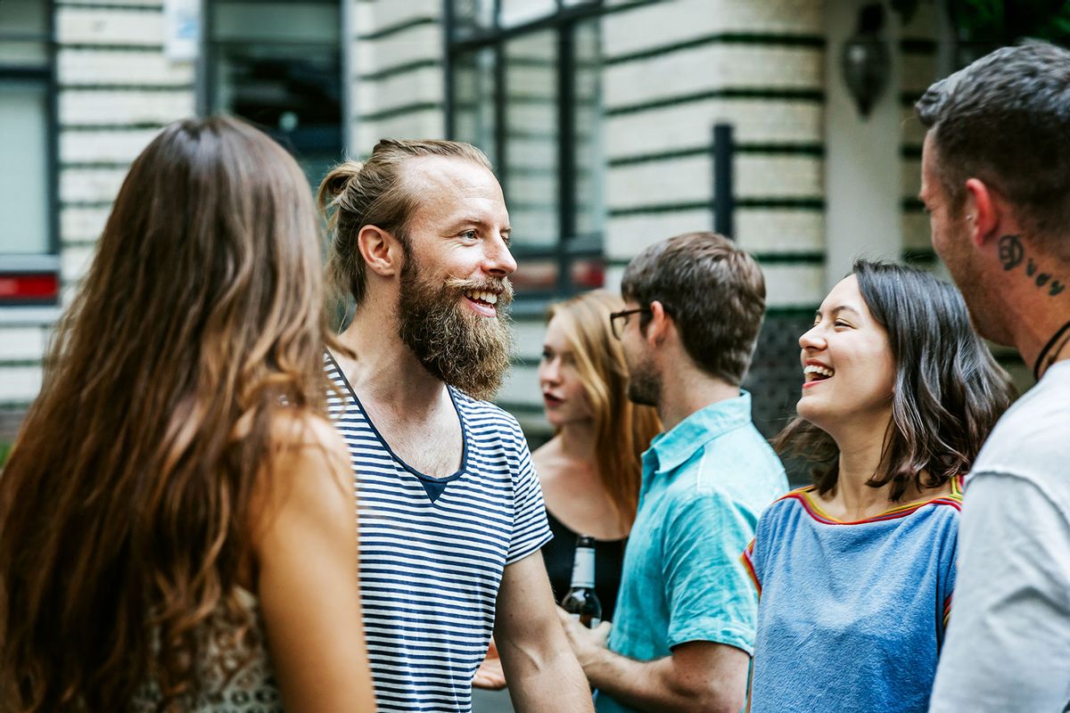 A young group of people meeting together at a barbecue are chatting and smiling as they greet each other (Getty Images/Hinterhaus Productions)