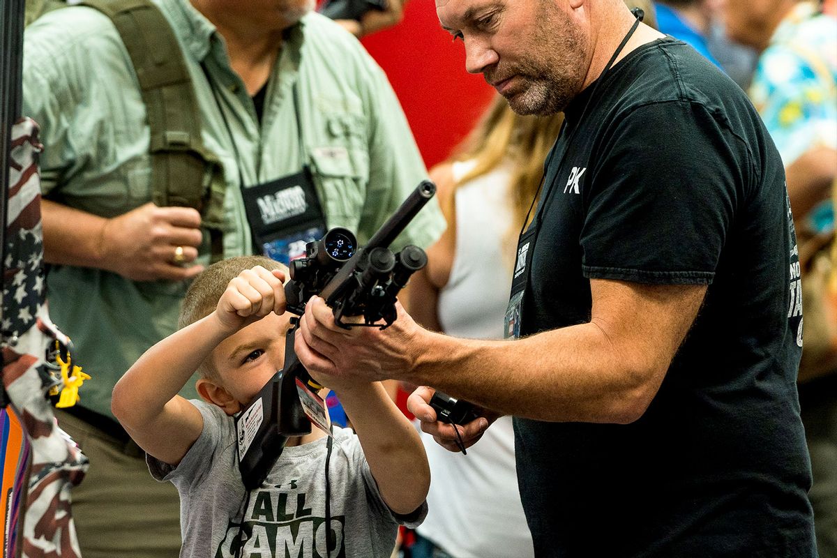 An attendee shows a young boy how to hold and load a gun during the National Rifle Association (NRA) annual convention at the Indiana Convention Center in Indianapolis, Indiana on Saturday, April 15, 2023. (Demetrius Freeman/The Washington Post via Getty Images)