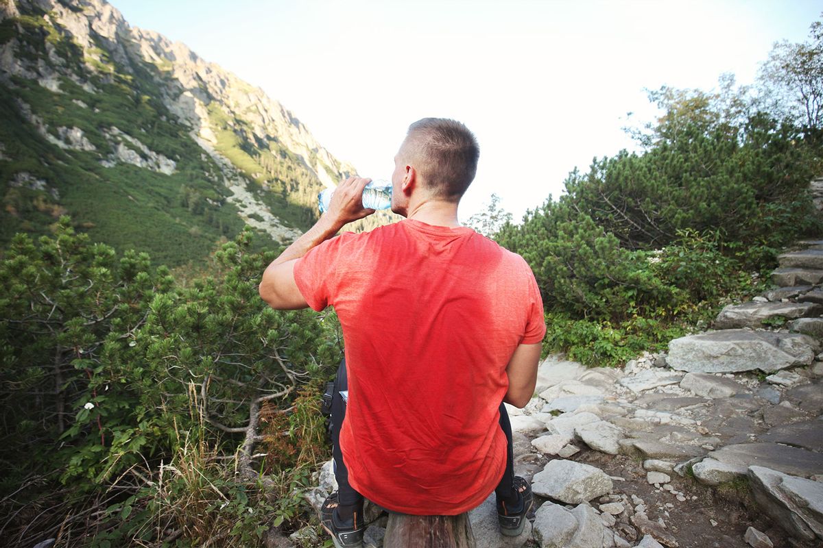Man after trekking with sweaty t-shirt drinking water against mountains (Getty Images/Stanislaw Pytel)