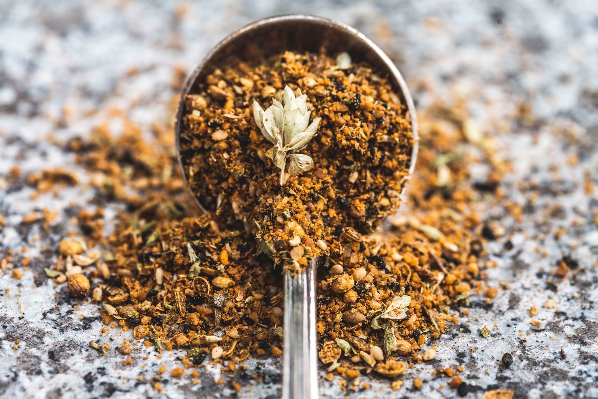 An antique spoon full of dukkah, a spice mix used in middle eastern cooking, spills out onto a stone table top. (Enrique Díaz / 7cero / Getty Images)