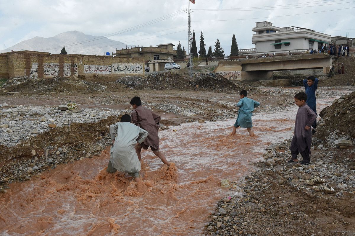 Children wade through floodwater near a damaged road following heavy rains on the outskirts of Quetta on April 15, 2024. (BANARAS KHAN/AFP via Getty Images)