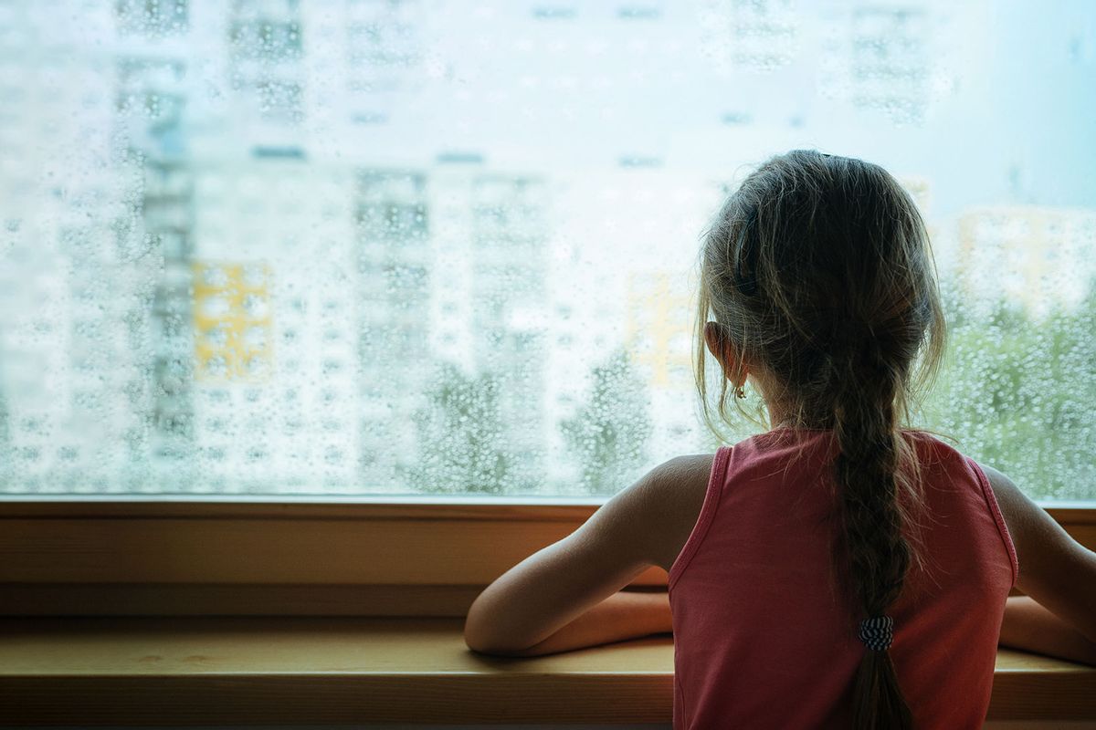 Little sad girl pensive looking through the rainy window. (Getty Images/Train_Arrival)