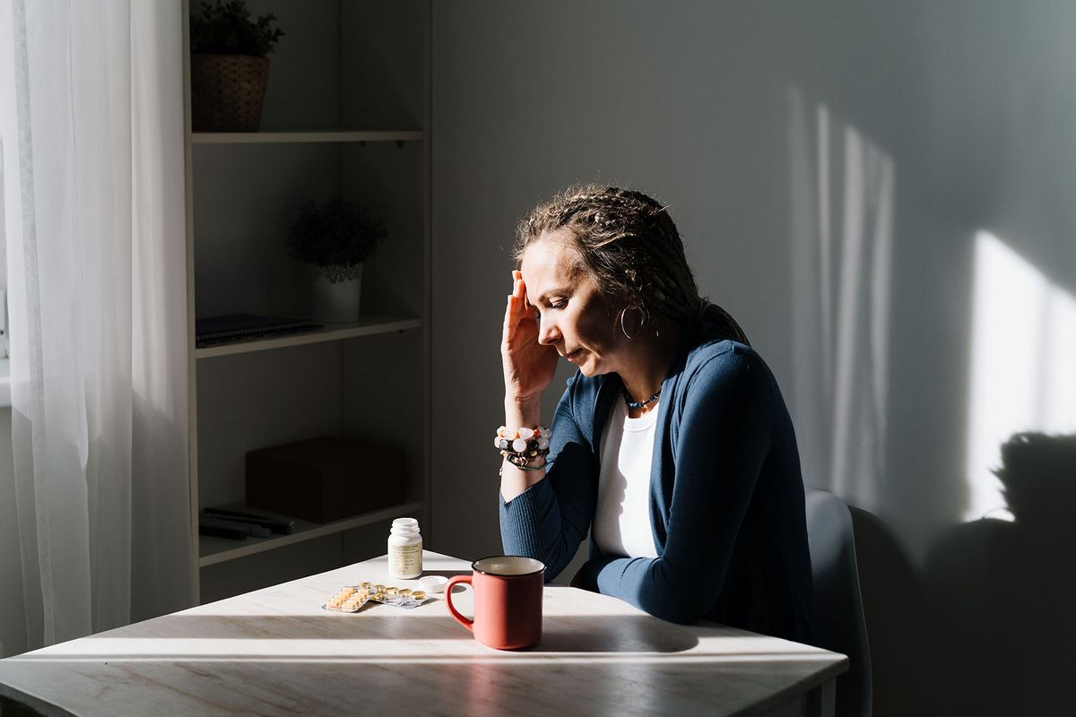 A Woman sitting at a table, upset. The first symptoms of incipient menopause are hypotension or hypertension, hot flashes. (Getty Images/Fiordaliso)