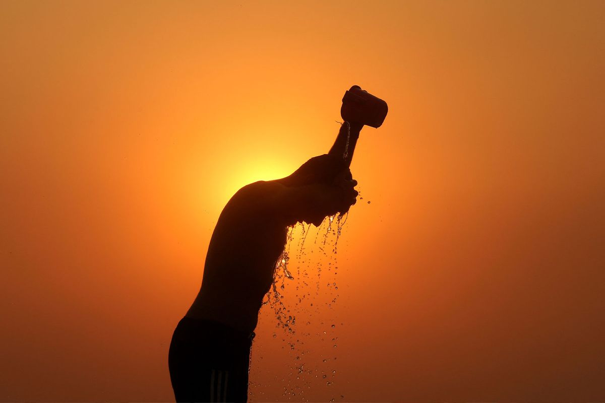 A labourer is silhouetted against the setting sun as he bathes on a hot summer day in Jammu on June 1, 2024. (MUKESH GUPTA/AFP via Getty Images)