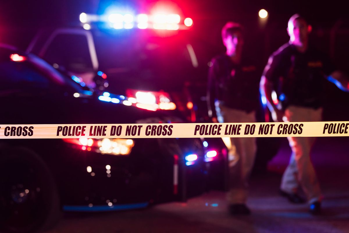 Two police officers standing in front of patrol cars, behind police tape. (Getty Images/kali9)