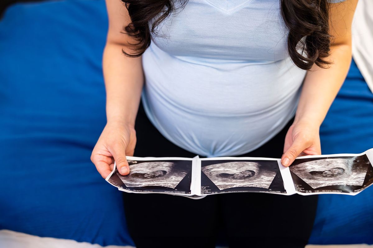 Pregnant woman in a medical exam room looking at her ultrasound pictures (Getty Images/adamkaz)