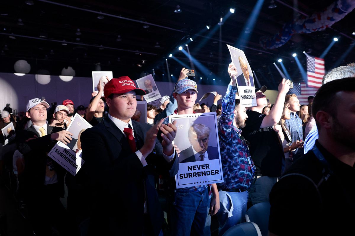People hold up placards with the mugshot of former US President and Republican presidential candidate Donald Trump as they wait for him to arrive to speak during the "Turning Point: The People's Convention" on June 15, 2024, at Huntington Place Convention Center in Detroit, Michigan. (JEFF KOWALSKY/AFP via Getty Images)