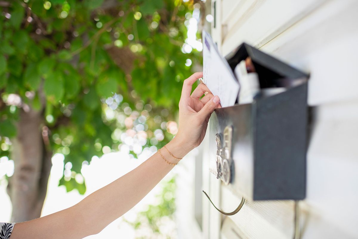 Woman's arm reaching for mail in residential mailbox mounted on exterior wall (Getty Images/Tony Anderson)