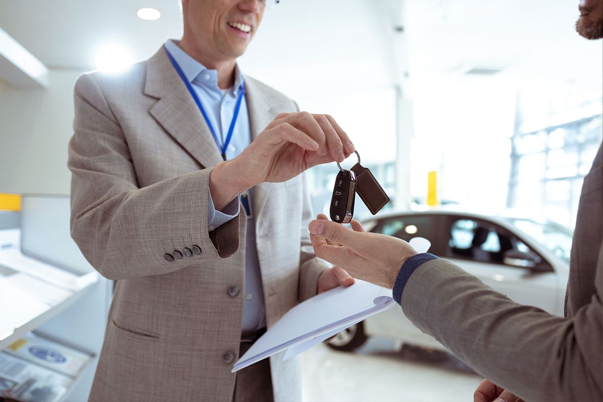 Man receiving car key of his new car in car dealership (Getty Images/blackCAT)