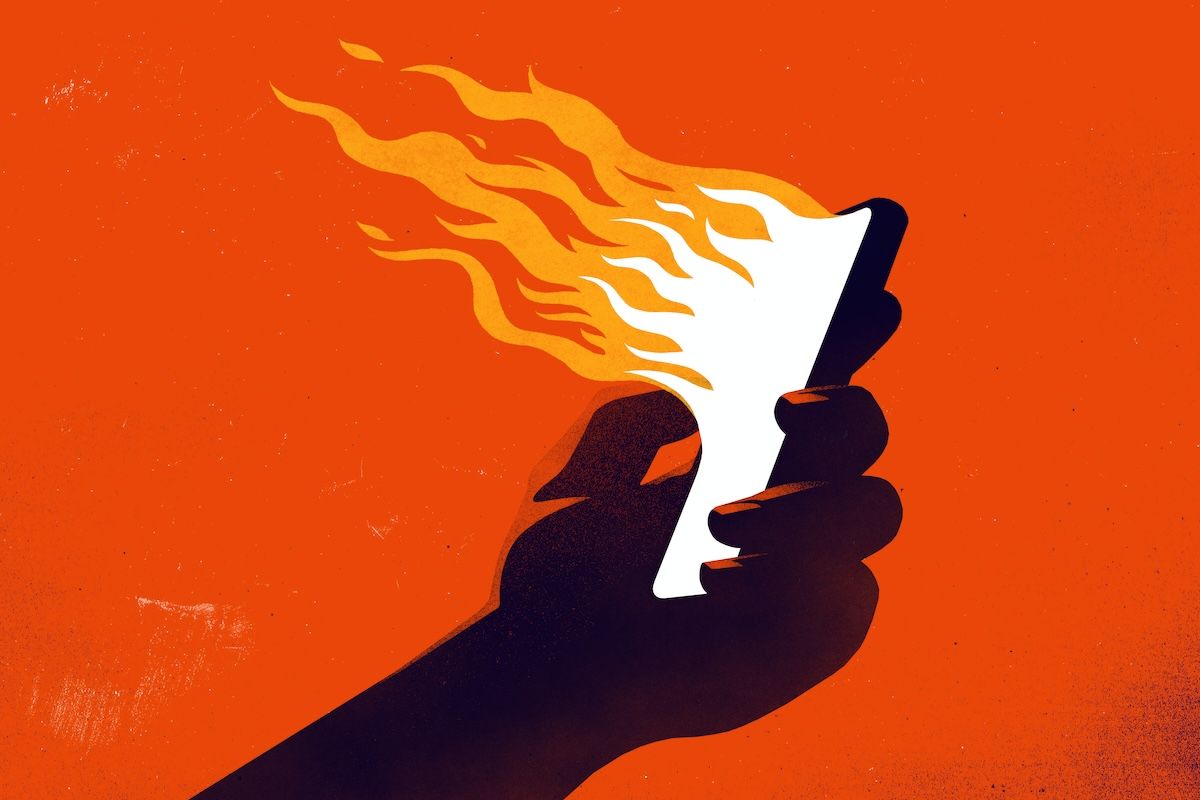 A hand holding a smartphone emanating flames.  (rob dobi / Getty Images)