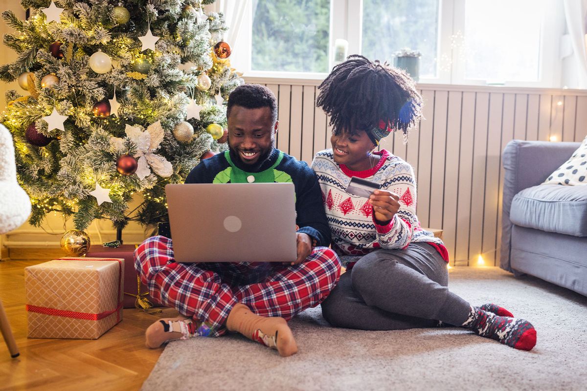 Young couple celebrating Christmas at home, online shopping and wearing Christmas sweaters. (Getty Images/svetikd)