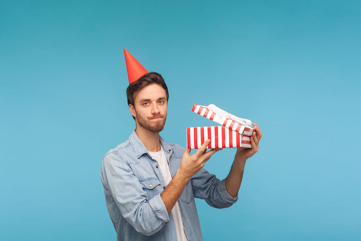 Frustrated man with party hat holding opened gift box (Getty Images/Khosrork)