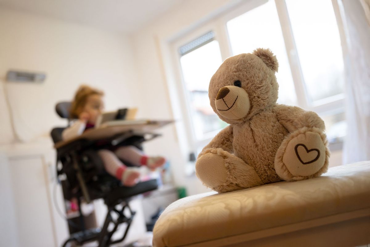 A teddy bear sits in a therapy chair in front of a child suffering from spinal muscular atrophy (SMA). (Sebastian Gollnow/picture alliance via Getty Images)