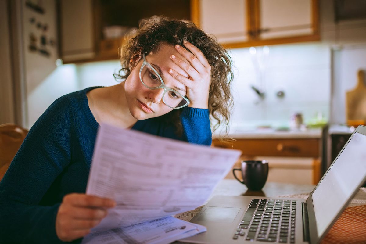 Woman going through bills, looking worried (Getty Images/urbazon)