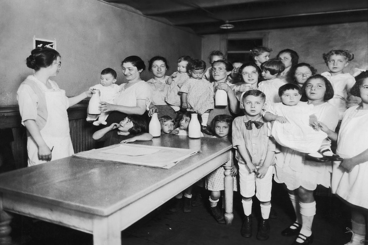 A group of mothers and children receive free milk from a Health Station on Madison Street in the Lower East Side of Manhattan, New York City, circa 1925. (Photo by FPG/Hulton Archive/Getty Images)