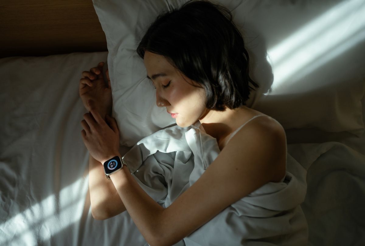 Woman sleeping peacefully in bed, wearing a smart watch to track her sleep patterns.  (Getty Images / whitebalance.space)