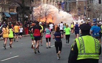Runners continue to run towards the finish line as an explosion erupts at the finish line of the Boston Marathon