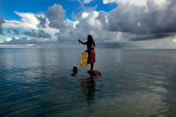 Binata Pinata stands on top of a rock holding a fish her husband Kaibakia just caught on Bikeman Islet, located off South Tarawa in the central Pacific island nation of Kiribati
