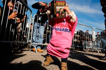 Photographers take pictures of a toddler with a book by Trump as they wait for the start of a rally with him at a car dealership in Portsmouth, New Hampshire