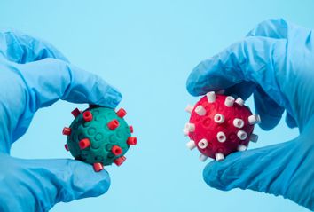 Scientists with surgical gloves holds two different Coronavirus of different color in the hand