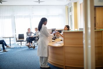Medical professional at reception with patients waiting in lobby at hospital