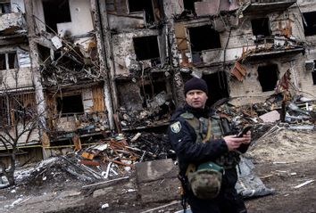 A Ukrainian police officer stands in front of a damaged residential block hit by an early morning missile strike