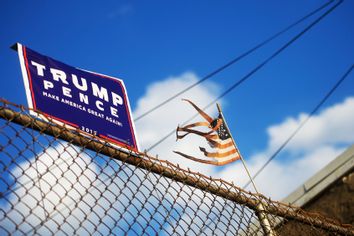 A tattered flag waves beside a Donald Trump campaign sign