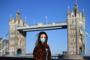 A member of the public poses for a photo in front of Tower Bridge whilst wearing a protective mask