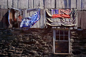 A pair of faded and torn Trump flags hang on an old barn