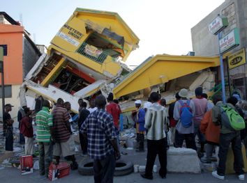 People look at a destroyed building in Port-au-Prince