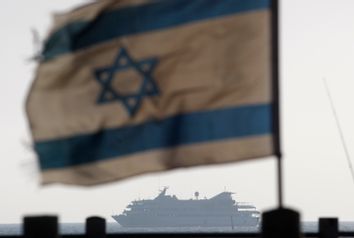 An Israeli flag flutters in the wind as a naval vessel escorts the Mavi Marmara to the Ashdod port